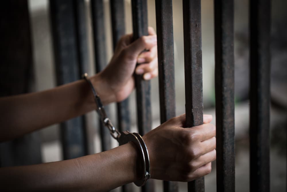 handcuffed young woman in a cage, representing themes of violence against women and human trafficking.